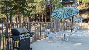 An outdoor patio area with a grill, metal chairs, and umbrellas.