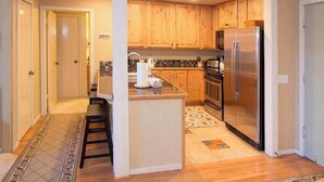 A modern kitchen with wooden cabinets, a stainless steel refrigerator, and a central island with bar stools.