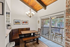 Un comedor con mesa de madera y bancos, una lámpara de araña y vistas al exterior a través de un ventanal.