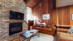 A cozy living room with a brick fireplace, leather sofa, and a television mounted on the wall.