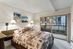 Un dormitorio con cama, mesitas de noche, ventana con vistas y lámparas de pared.