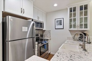 A modern kitchen with stainless steel appliances, white cabinetry, a granite countertop, and a built-in oven.