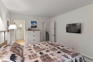 Une chambre à coucher comprenant un lit, une commode, un téléviseur et une porte donnant sur une salle de bain.