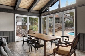 Un patio couvert avec une table et des chaises, de grandes portes-fenêtres coulissantes et une vue sur une piscine.