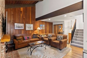 Un salon chaleureux avec un canapé en cuir marron, deux fauteuils, une table basse et une cheminée.