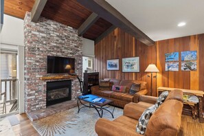 A cozy living room with a brick fireplace, leather sofa, and wooden panel walls. - Chamonix Retreat | Nearby Outdoor Activities! (Mammoth Lakes)
