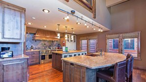 A spacious kitchen with wooden cabinets, a large island with bar stools, and a stone countertop. - Group Townhouse | 4 Ensuite Beds, Den, Sleeps 12 (Mammoth Lakes)