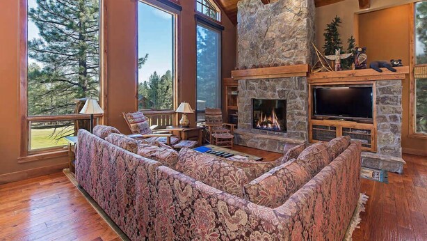 A cozy living room with a stone fireplace, large windows, and a patterned sofa. - Group Townhouse | 4 Ensuite Beds, Den, Sleeps 12 (Mammoth Lakes)