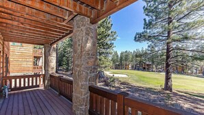 A wooden deck with stone pillars, a view of a golf course, and surrounding trees. - Group Townhouse | 4 Ensuite Beds, Den, Sleeps 12 (Mammoth Lakes)
