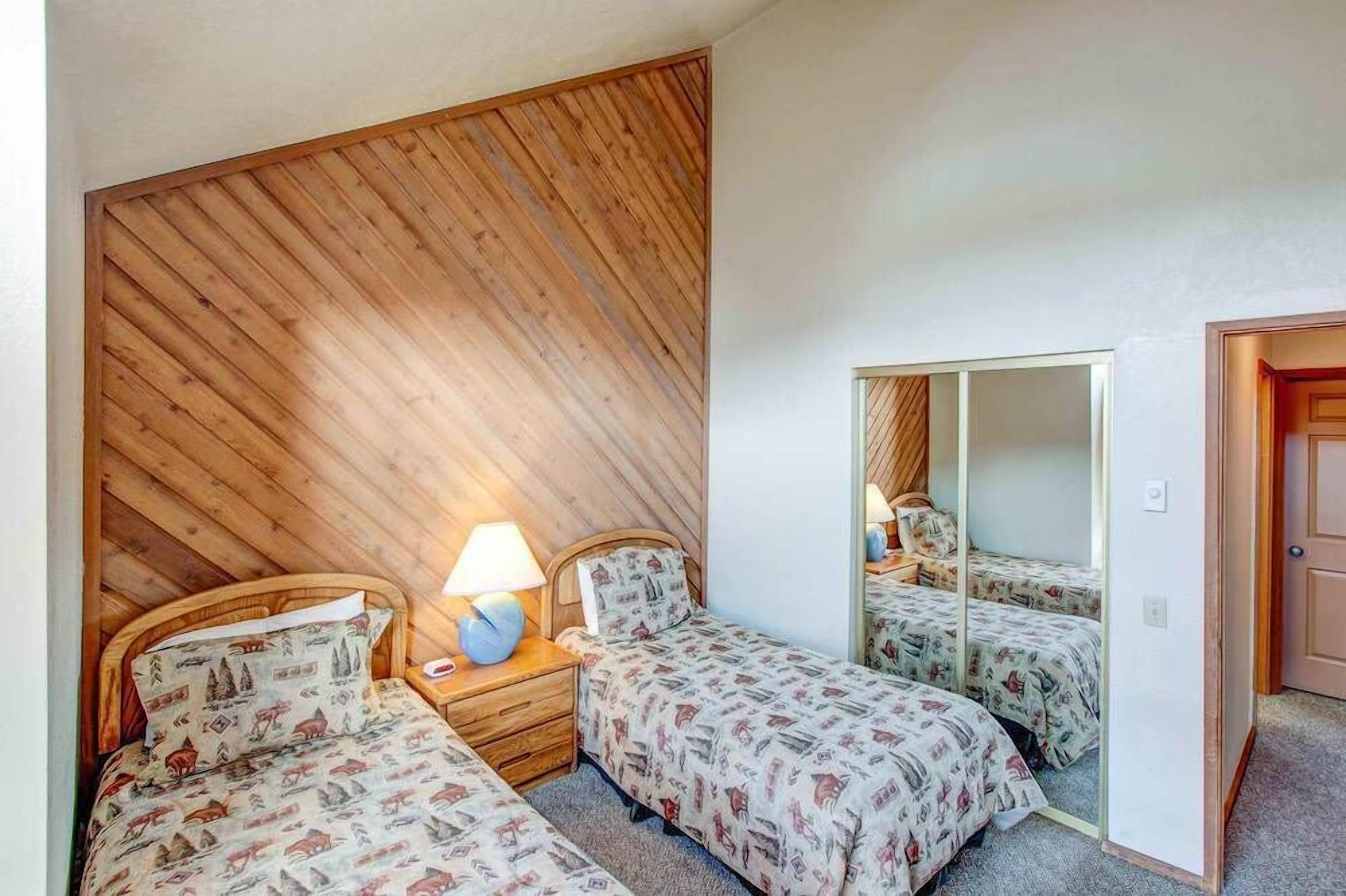 Een slaapkamer met twee bedden, een wand van houten latten, een spiegel en een nachtkastje met een lamp.