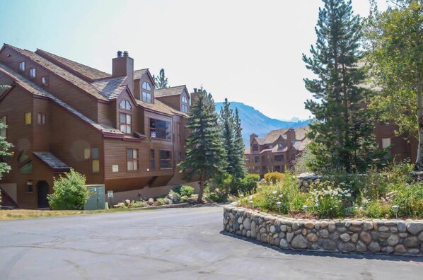 A multi-story building with a sloped roof, large windows, and a stone foundation. - Aspen Creek #204 | Near Golf, Fishing & Hiking (Mammoth Lakes)