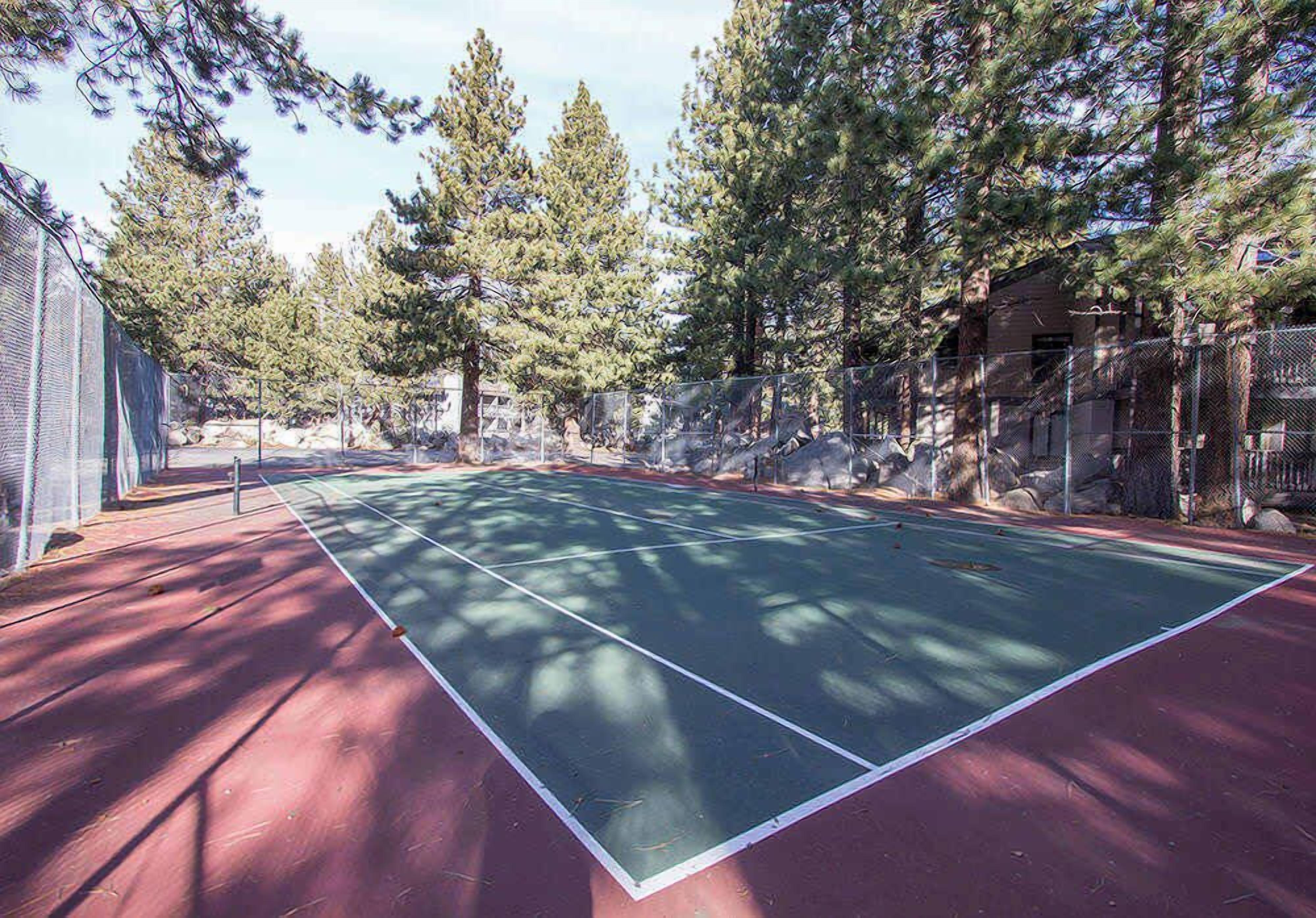 An outdoor tennis court surrounded by trees and a fence.