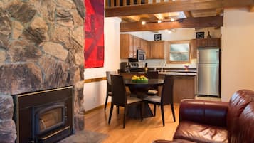 A stone fireplace, a dining area with a table and chairs, a kitchen with wooden cabinets and a refrigerator, and a leather couch.