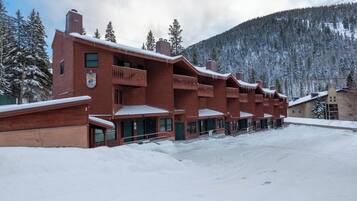 A row of wooden cabins with balconies, set against a snowy mountain backdrop.