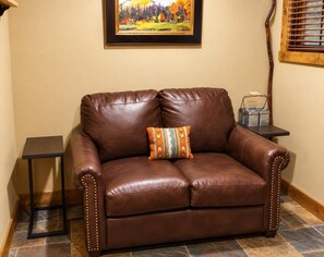 A brown leather sofa with a patterned cushion, a small side table, and a framed painting on the wall.