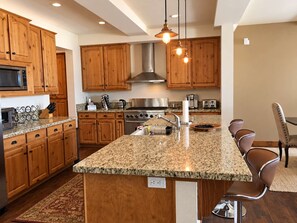 A kitchen with wooden cabinets, granite countertops, stainless steel appliances, and pendant lighting.