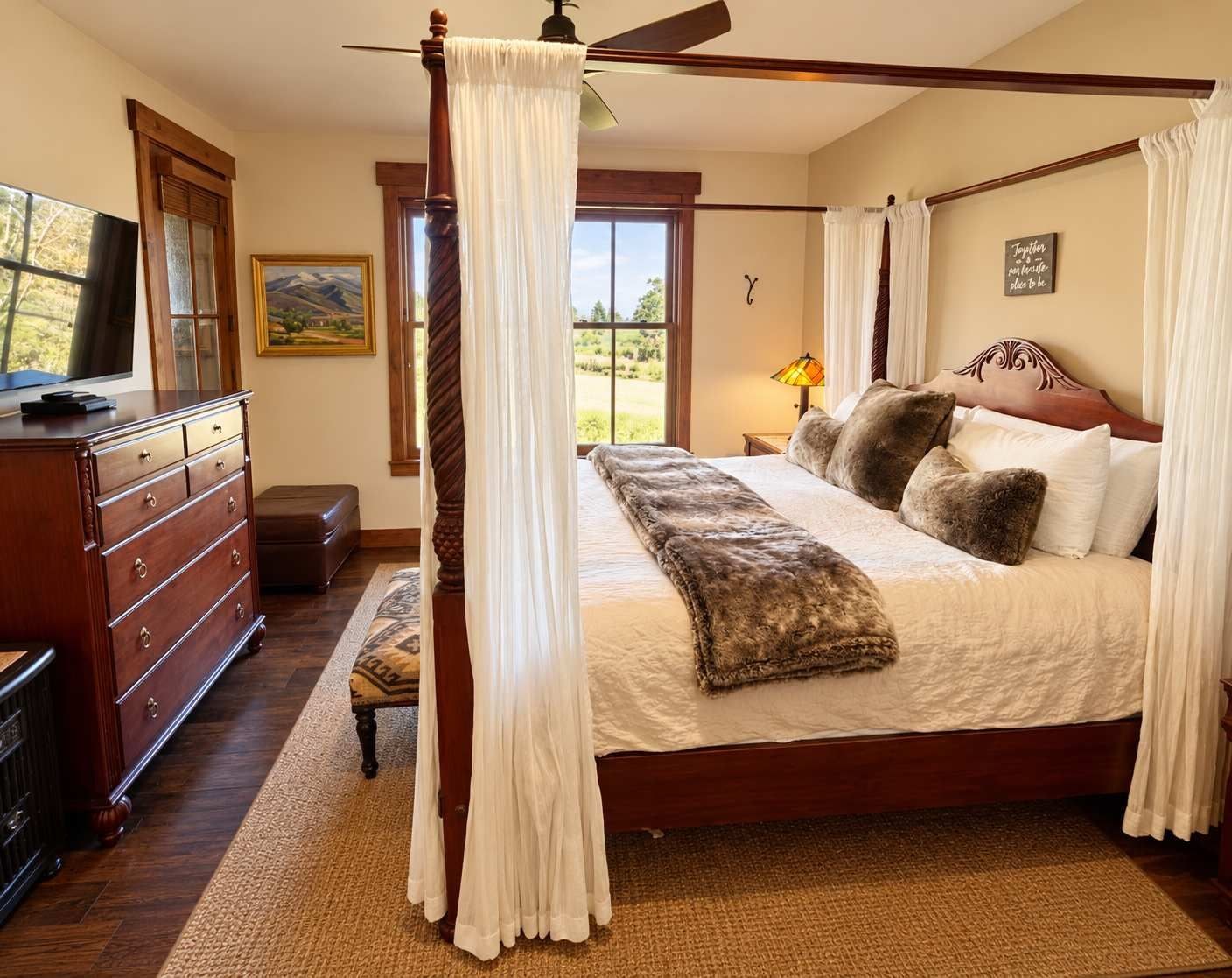 A bedroom with a four-poster bed, a wooden dresser, a television, and a painting on the wall.