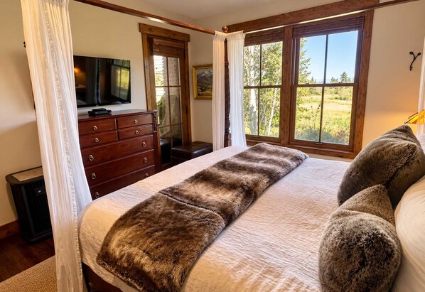 A bedroom with a large bed, a television on a dresser, and a window with a view of trees.