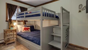 A bunk bed room with a desk and chair, a window with curtains, and a wall decoration.