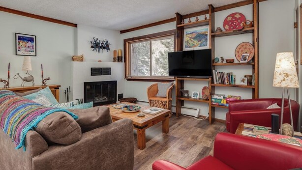 A cozy living room with a fireplace, comfortable seating, a television, and a bookshelf with various items.