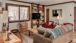 A cozy living room with a wooden bookshelf, a red armchair, a brown sofa, and a television.
