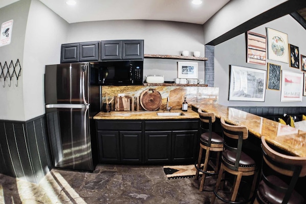 Una cocina moderna con armarios negros, electrodomésticos de acero inoxidable, encimera de mármol y una zona de bar con taburetes.