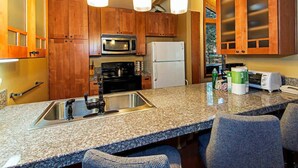 A kitchen with granite countertops, wooden cabinets, a stainless steel sink, a microwave, a refrigerator, and a toaster.
