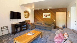 Ein Wohnzimmer mit Flachbildfernseher, Couch, Couchtisch aus Holz und einem gemusterten Teppich.