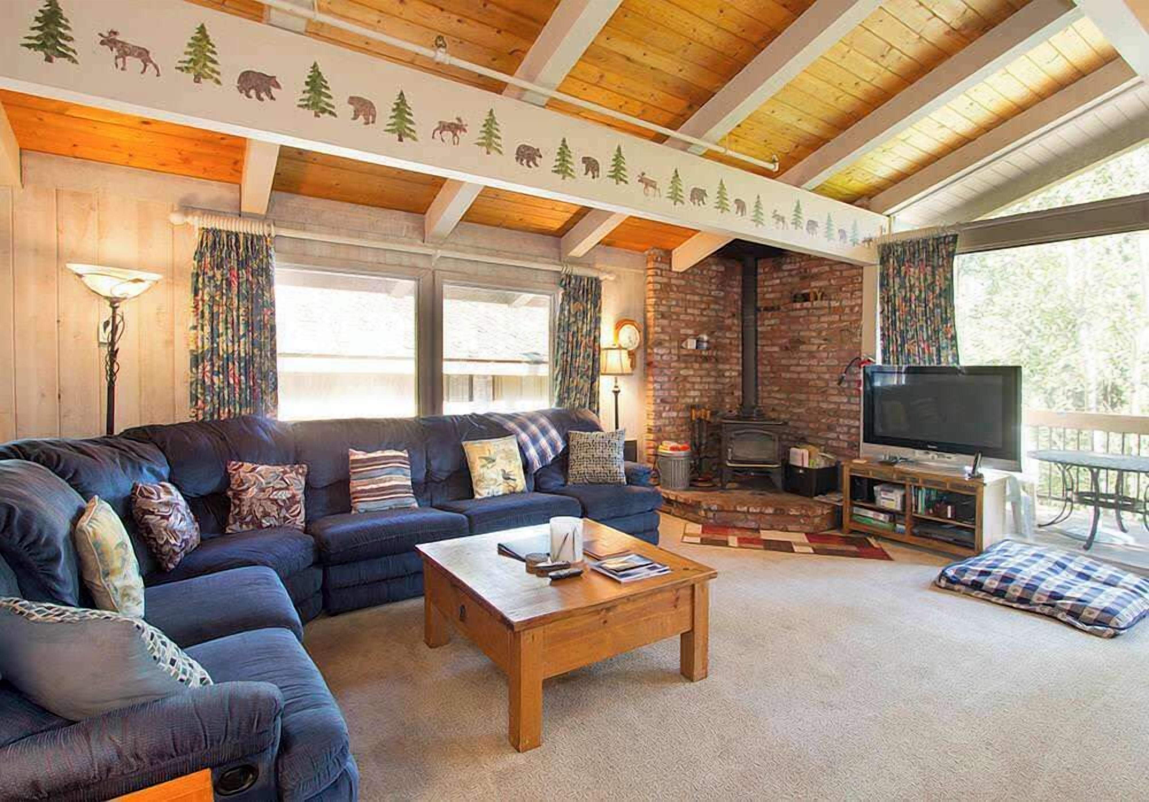 A cozy living room with a blue sofa, a wooden coffee table, a brick fireplace, and a television.