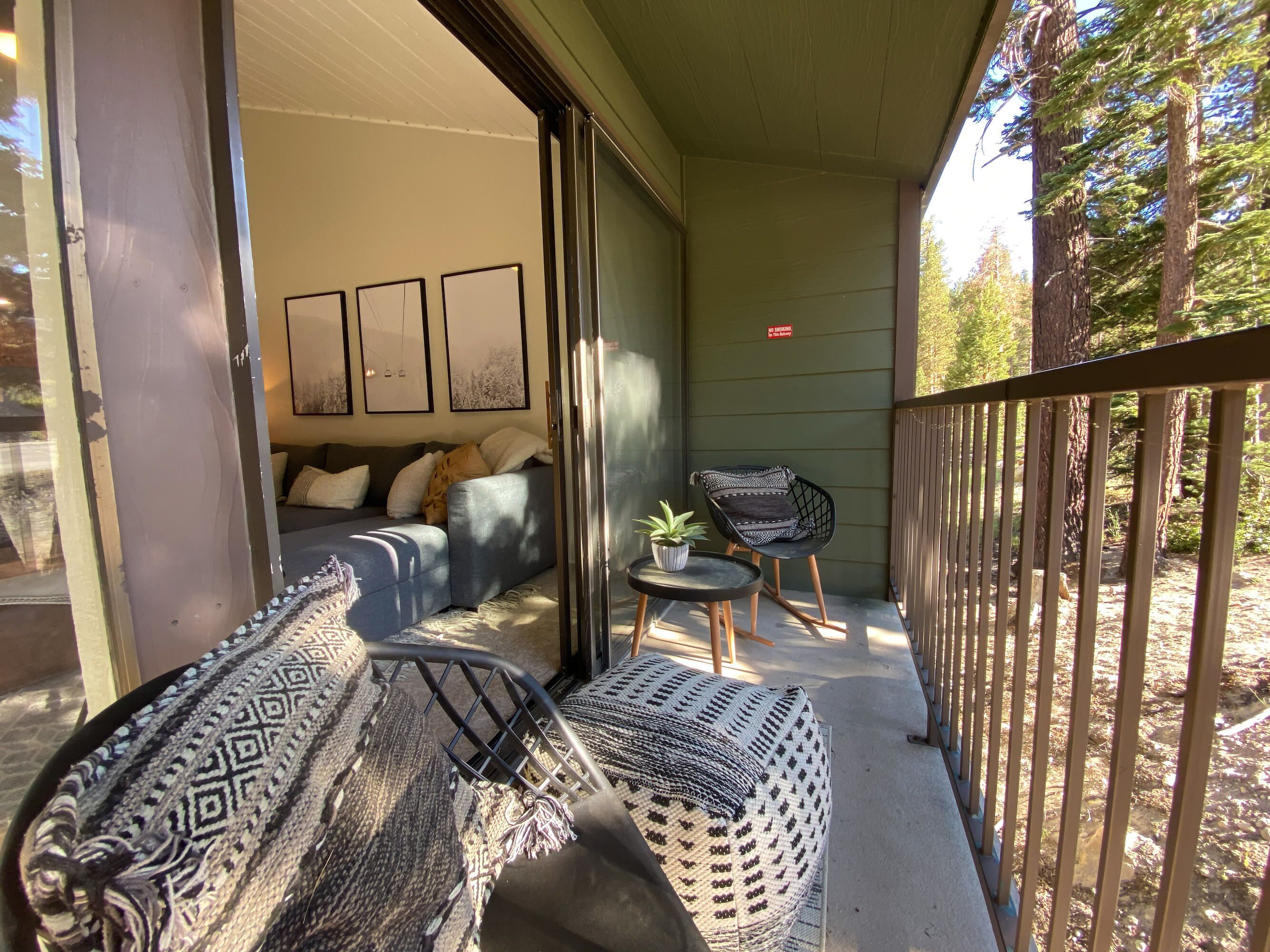 A cozy outdoor seating area with a sofa and chairs, a small table with a plant, and a view of a forest.