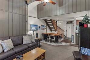 A modern living room with a sofa, coffee table, and a dining area with a wooden table and chairs. - Escape to The Summit | Cozy Mammoth Getaway (Mammoth Lakes)