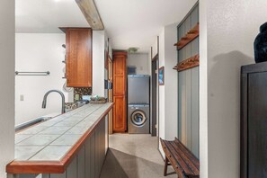 A narrow hallway with a kitchen area, a washing machine, and a bench. - Escape to The Summit | Cozy Mammoth Getaway (Mammoth Lakes)