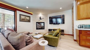 Ein Wohnzimmer mit Sofa, Sesseln, Couchtisch und einem an der Wand befestigten Flachbildfernseher.