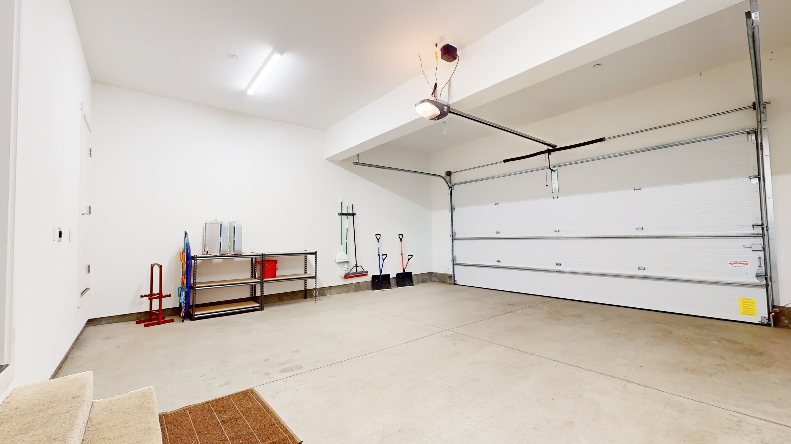 A spacious garage with a concrete floor, a metal shelving unit, and various tools hanging on the wall.