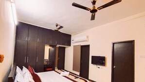 A bedroom with a bed, dark cabinets, a ceiling fan, an air conditioning unit, a TV, and a door. - Neighbour Inn Elite (Chennai)