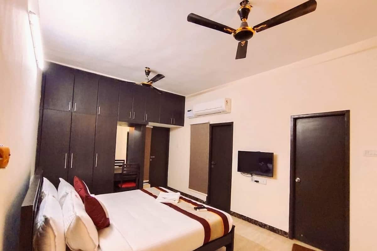 A bedroom with a bed, dark cabinets, a ceiling fan, an air conditioning unit, a TV, and a door.