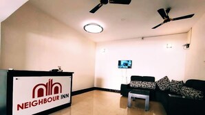 A reception area with a 'Neighbour Inn' sign, a sofa set, a small table, and ceiling fans. - Neighbour Inn Elite (Chennai)