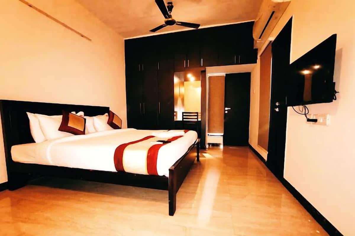 A hotel room with a bed, a ceiling fan, a TV mounted on the wall, and a wooden floor.