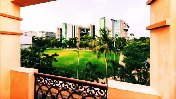 A balcony with a view of a modern building complex, a green lawn, and palm trees. - Neighbour Inn Elite (Chennai)
