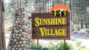 A wooden sign with the text "Sunshine Village" surrounded by a stone wall and greenery. - Sleeps 8 w Loft | 3 Baths, Hot Tub & Tennis (Mammoth Lakes)