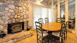 A stone fireplace, wooden dining table, and chairs in a room with a stone wall and wooden flooring. - Sleeps 8 w Loft | 3 Baths, Hot Tub & Tennis (Mammoth Lakes)