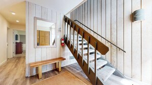 A staircase with a wooden handrail and white steps, a wooden bench, a fire extinguisher, and a mirror on the wall.