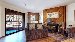 Una sala de estar acogedora con chimenea, paredes de madera y un ventanal grande con vistas a una terraza.