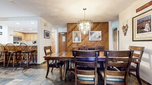 Un comedor con mesa y sillas de madera, una araña y cuadros en las paredes.