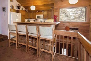 L’intérieur d’un chalet en bois comprend une cuisine, un coin bar et une fenêtre donnant sur les arbres.