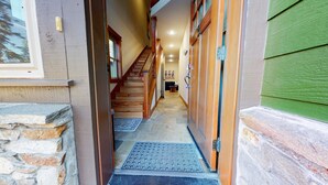 Un pasillo con una escalera de madera, paredes de piedra y una puerta verde.