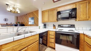 Une cuisine moderne avec des meubles en bois, un évier en acier inoxydable, un lave-vaisselle encastré, une cuisinière et un four à micro-ondes.