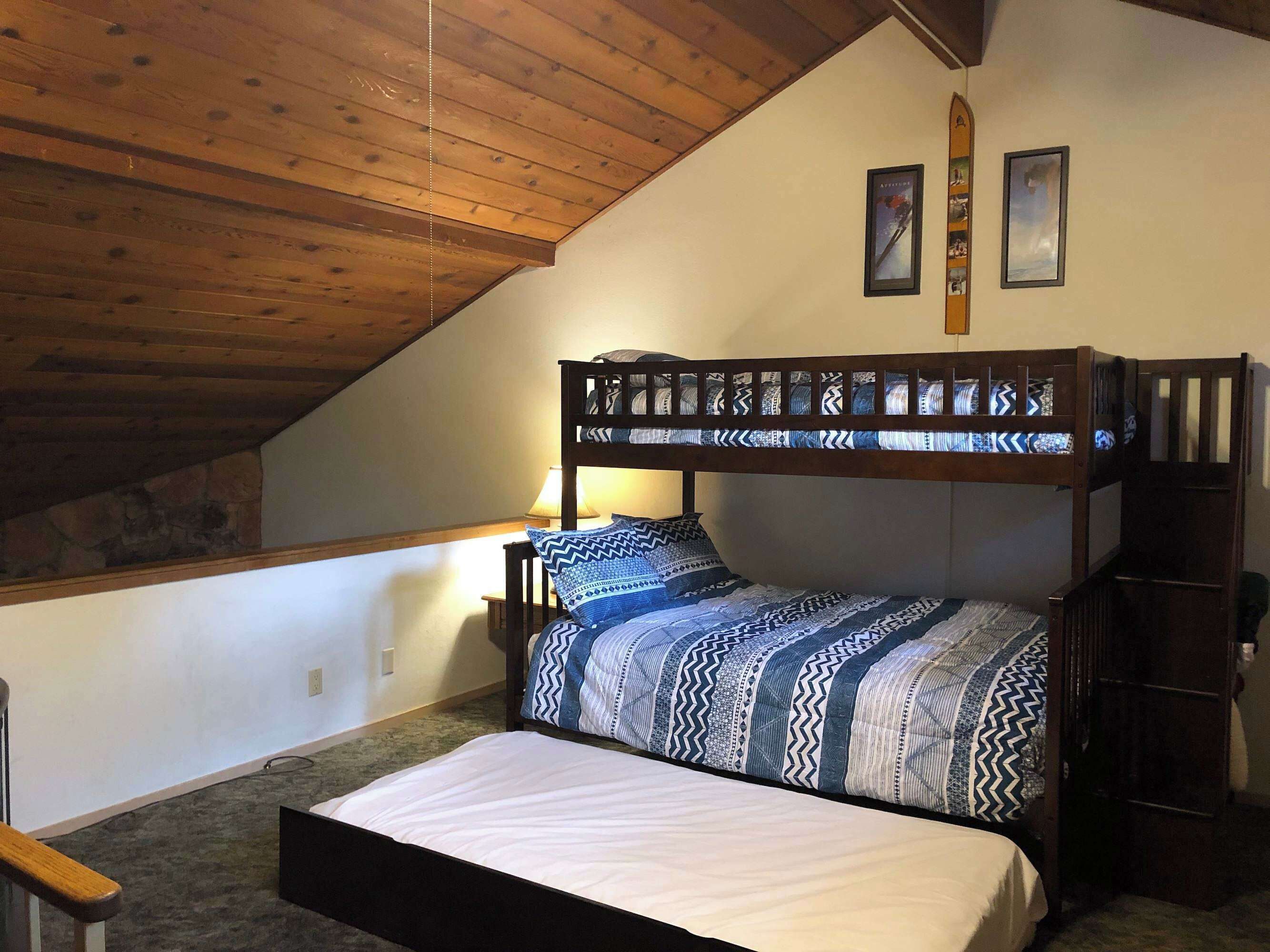 A bedroom with a bunk bed, a single bed, a lamp, and two framed pictures on the wall.