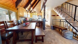 A spacious kitchen with wooden cabinets, a dining area with a large table and benches, and a staircase with a unique carpeted design.