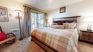 A bedroom with a large bed, a wooden nightstand, a chair, a radiator, and a window with curtains.